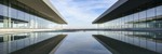 Futuristic glass building mirrored on a still water surface with a cloudy sky.